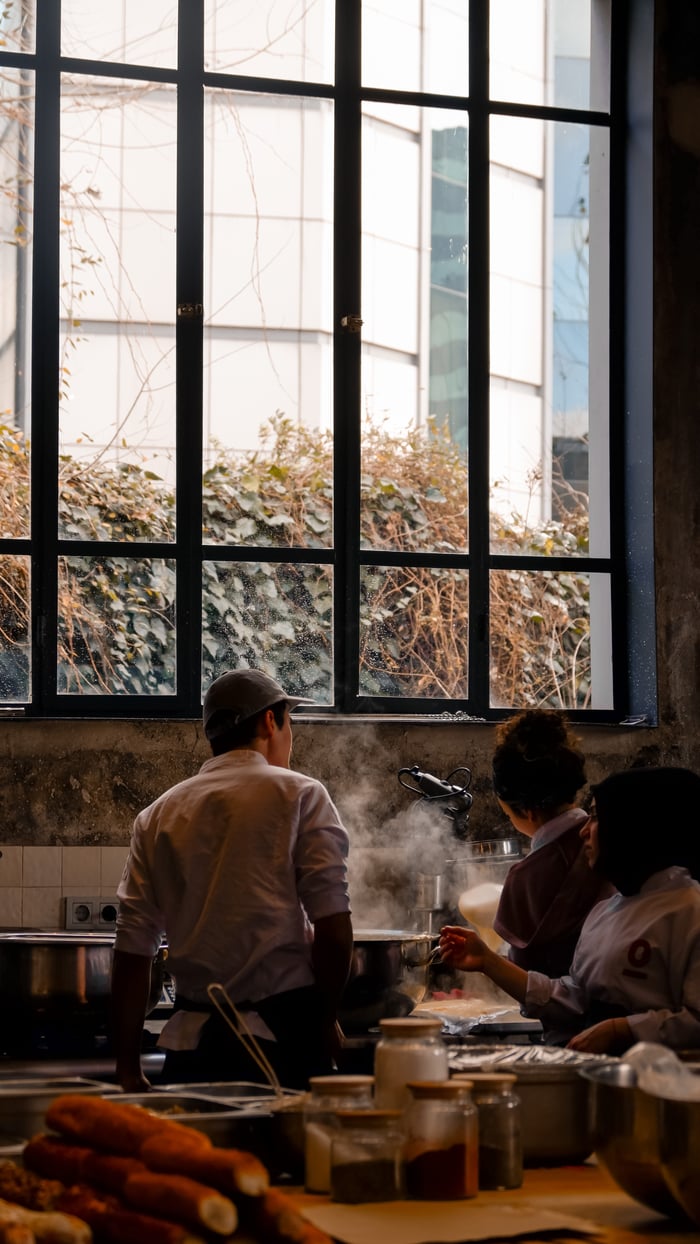 services-04 Professional chefs work together preparing meals in a restaurant kitchen with steam rising.