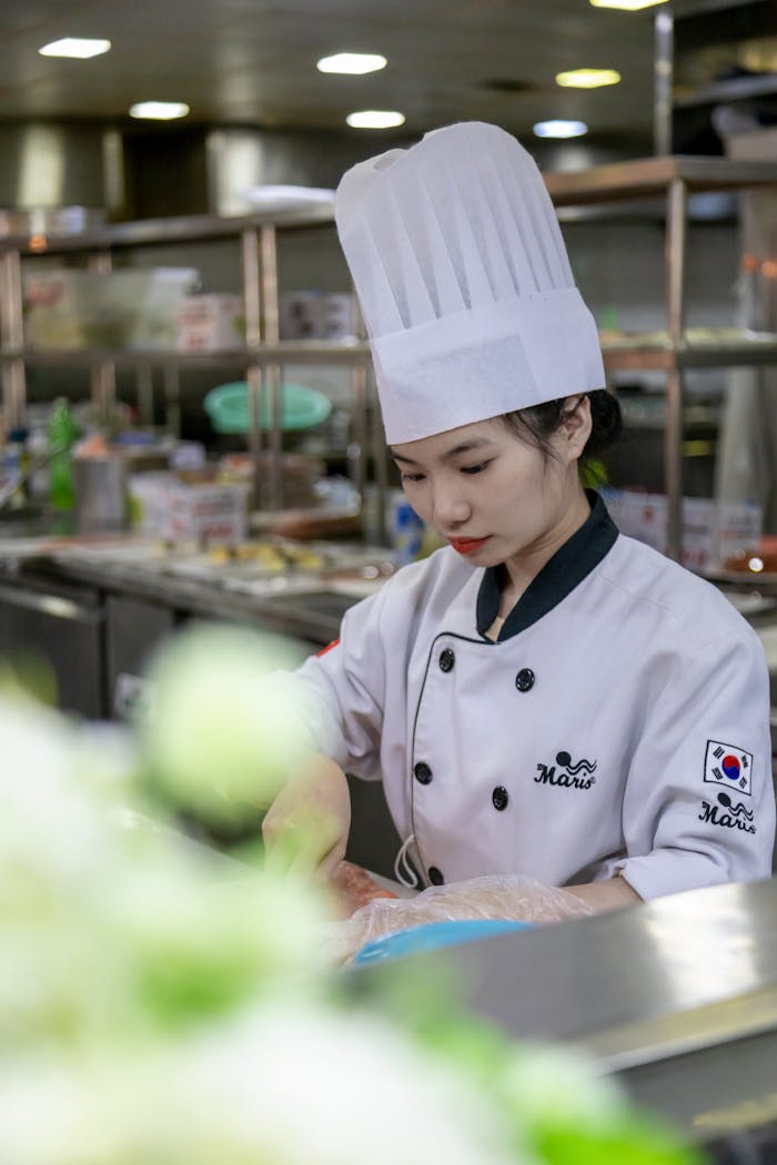 services-03 Chef in a white uniform and hat focusing on preparing food in a commercial kitchen setting.