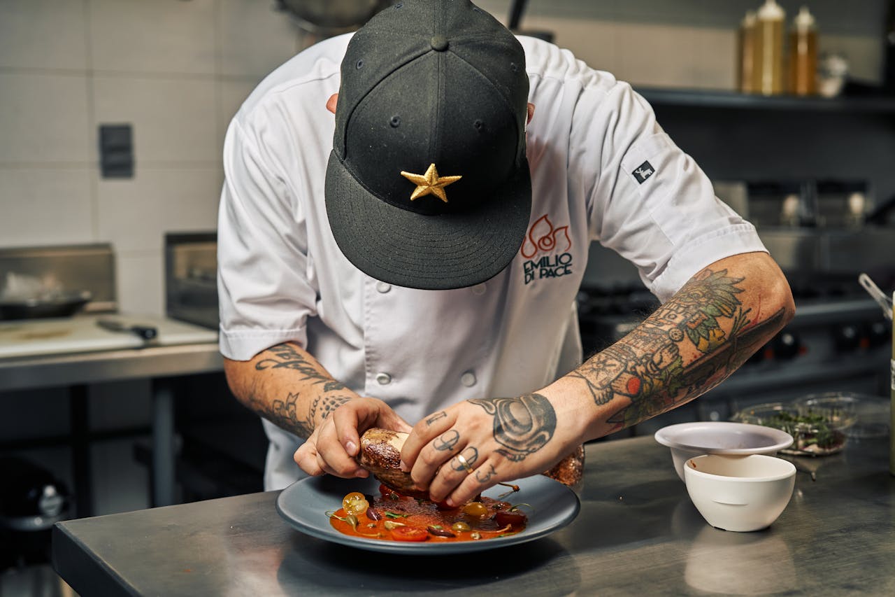 team-04 Tattooed chef expertly plates a gourmet dish with precision and skill in a restaurant kitchen.