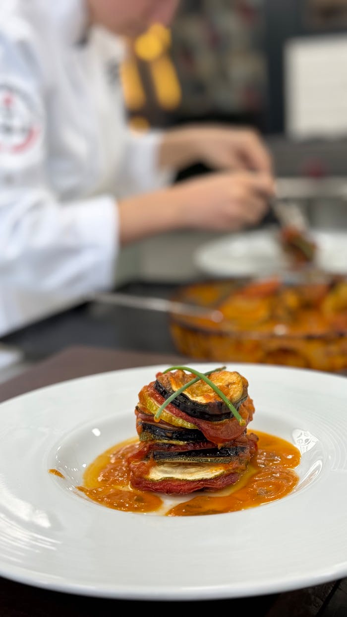 services-02 Elegant gourmet ratatouille plated in a professional kitchen setting with a chef in the background.
